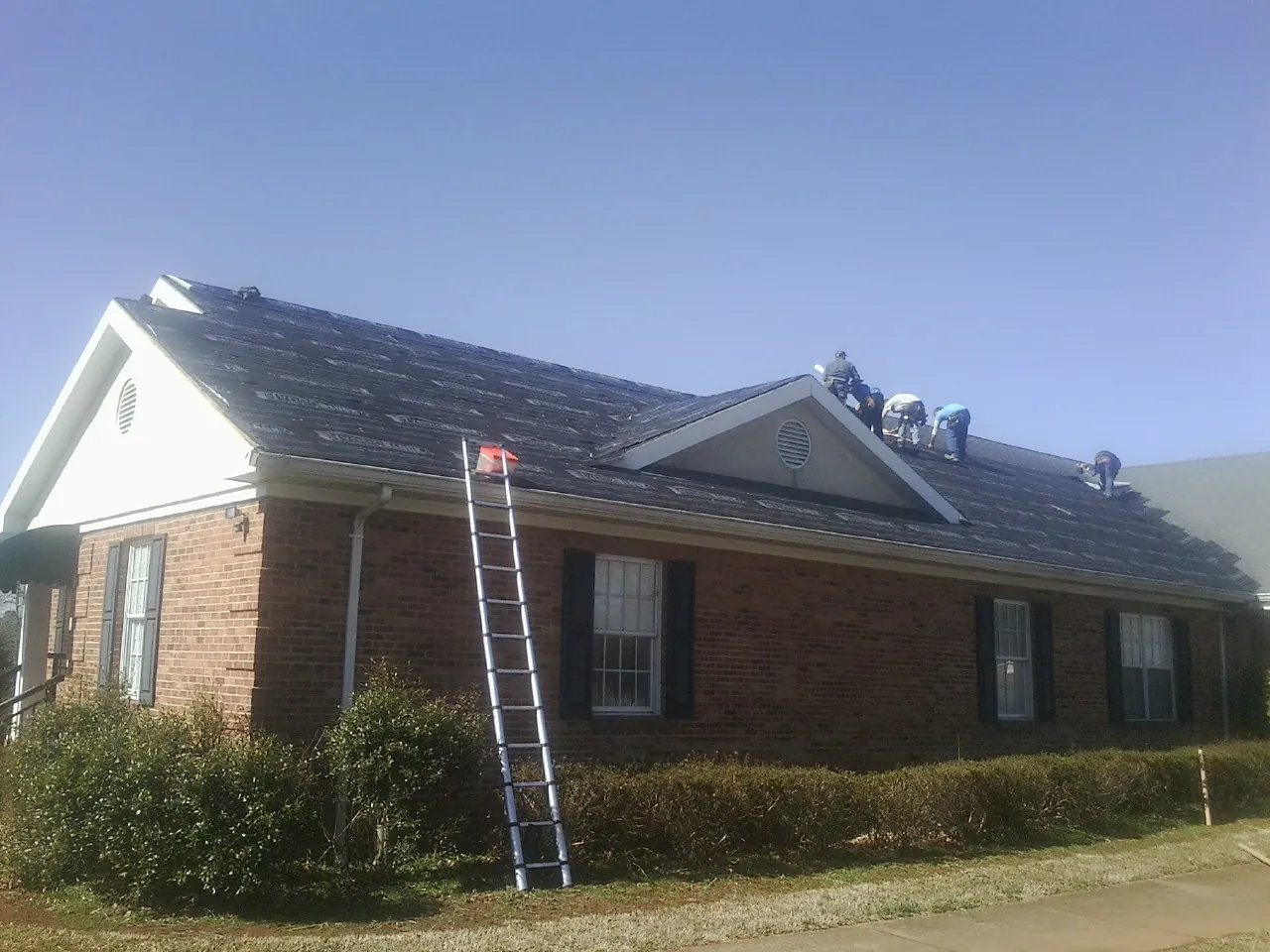 Crew tearing shingles off a brick ranch roof with a ladder set — Emergency Roof Repair work by our crew in Johnston