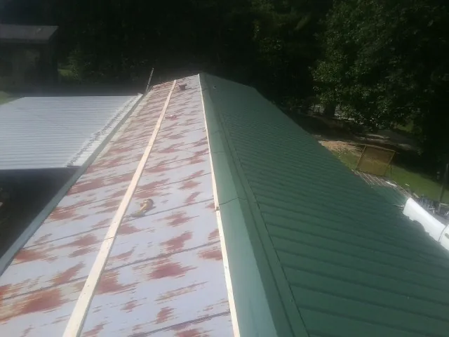 Old rusted panels beside newly installed green metal roofing — Wind Damage Roof Repair by Roofing Brothers in Johnston