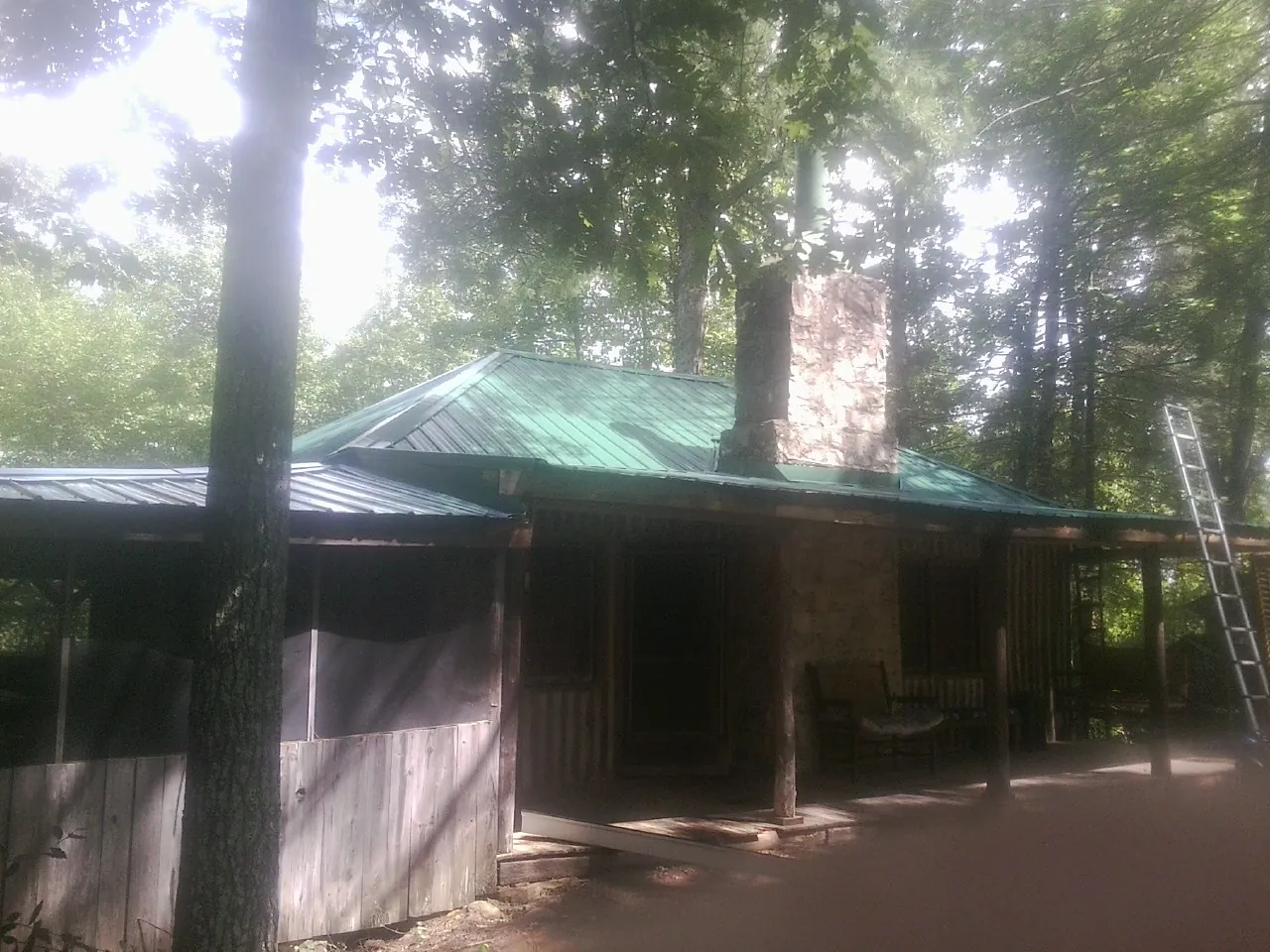 Green metal roof and stone chimney above a log cabin porch in Johnston