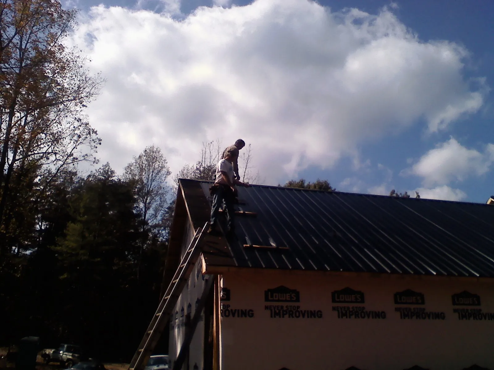 Roofer fastening dark metal panels high against a cloudy sky, from a Roof Inspection job in Johnston
