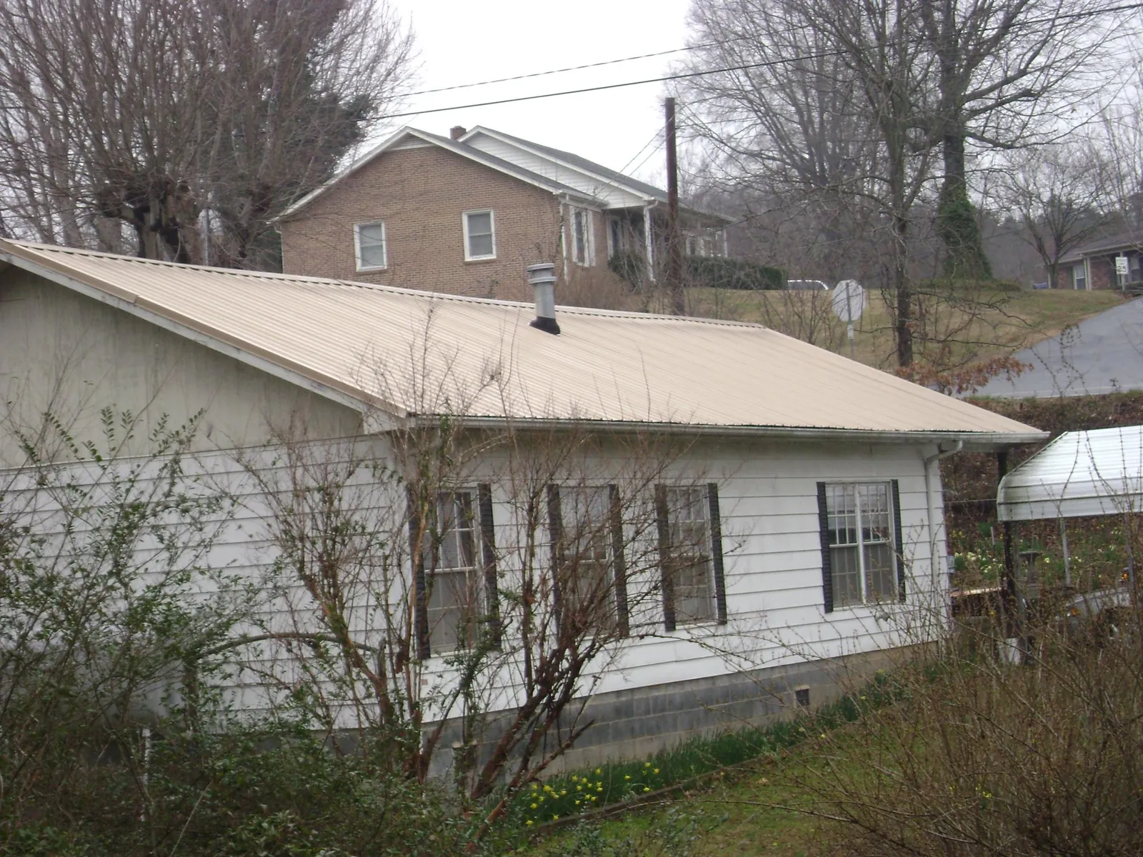 Tan metal roof on a white sided house set into a hillside — Commercial Roofing by Roofing Brothers in Johnston